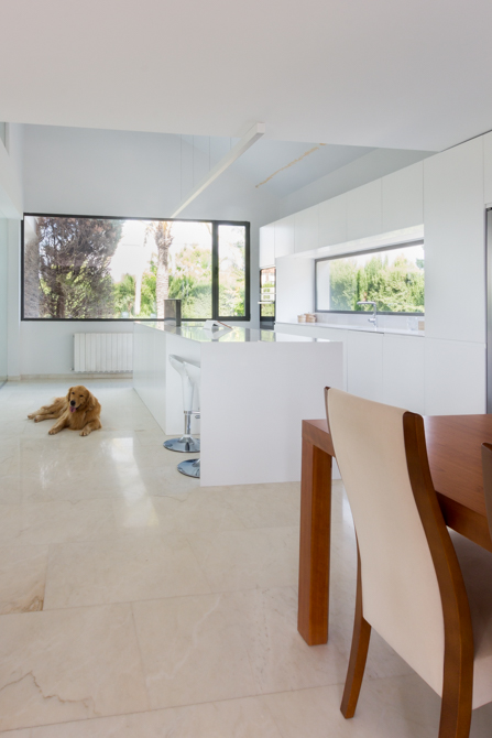 Cocina moderna blanca con isla con ventana en vivienda mediterránea. Chiralt Arquitectos Valencia
