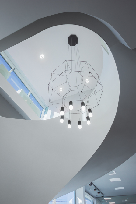 Escalera blanca en espiral en hall de oficinas modernas con lampara moderna de vibia