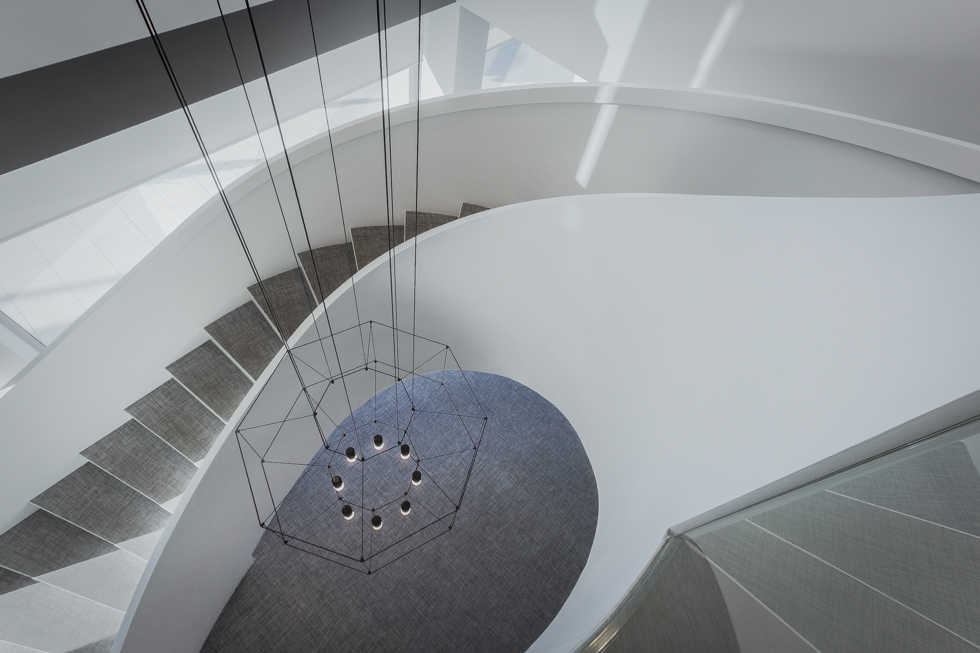 Escalera blanca y minimalista en espiral en hall de oficinas modernas con lampara moderna de vibia