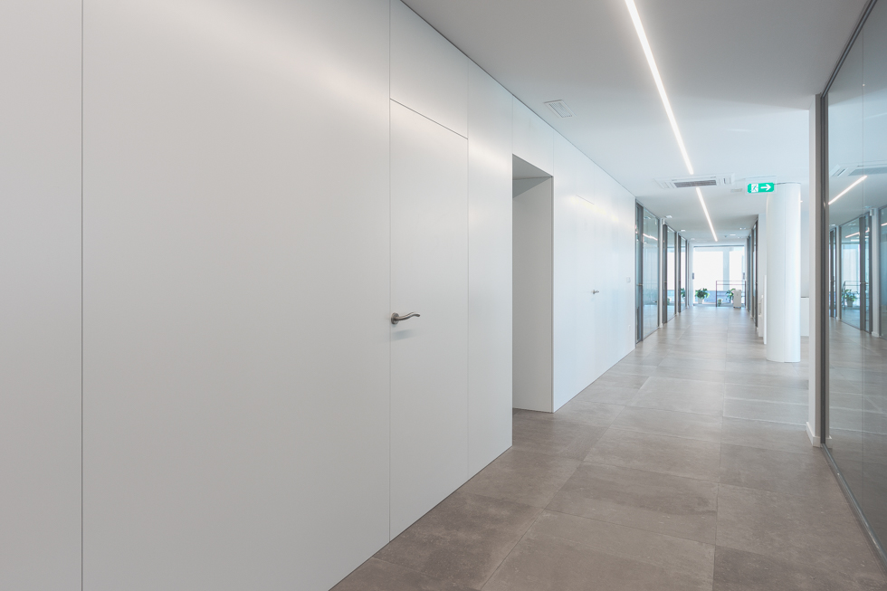 Pasillo de oficinas modernas con puertas blancas, puertas de cristal y suelo gris